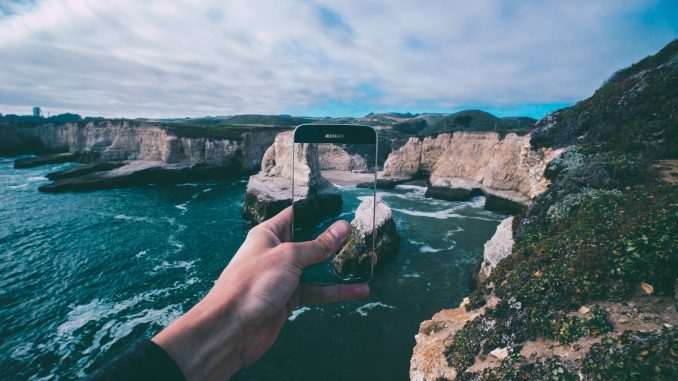 Mann fotografiert mit Smartphone eine Klippe.